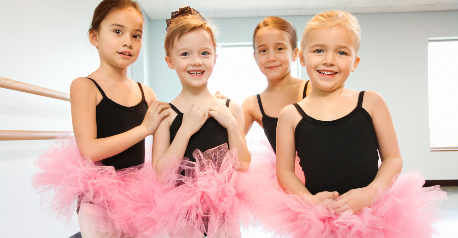 Group of young ballet students in a dance studio wearing pastel tutus and ballet shoes, practicing at the barre together, illustrating beginner ballet class for kids and supportive guidance for new dance parents.